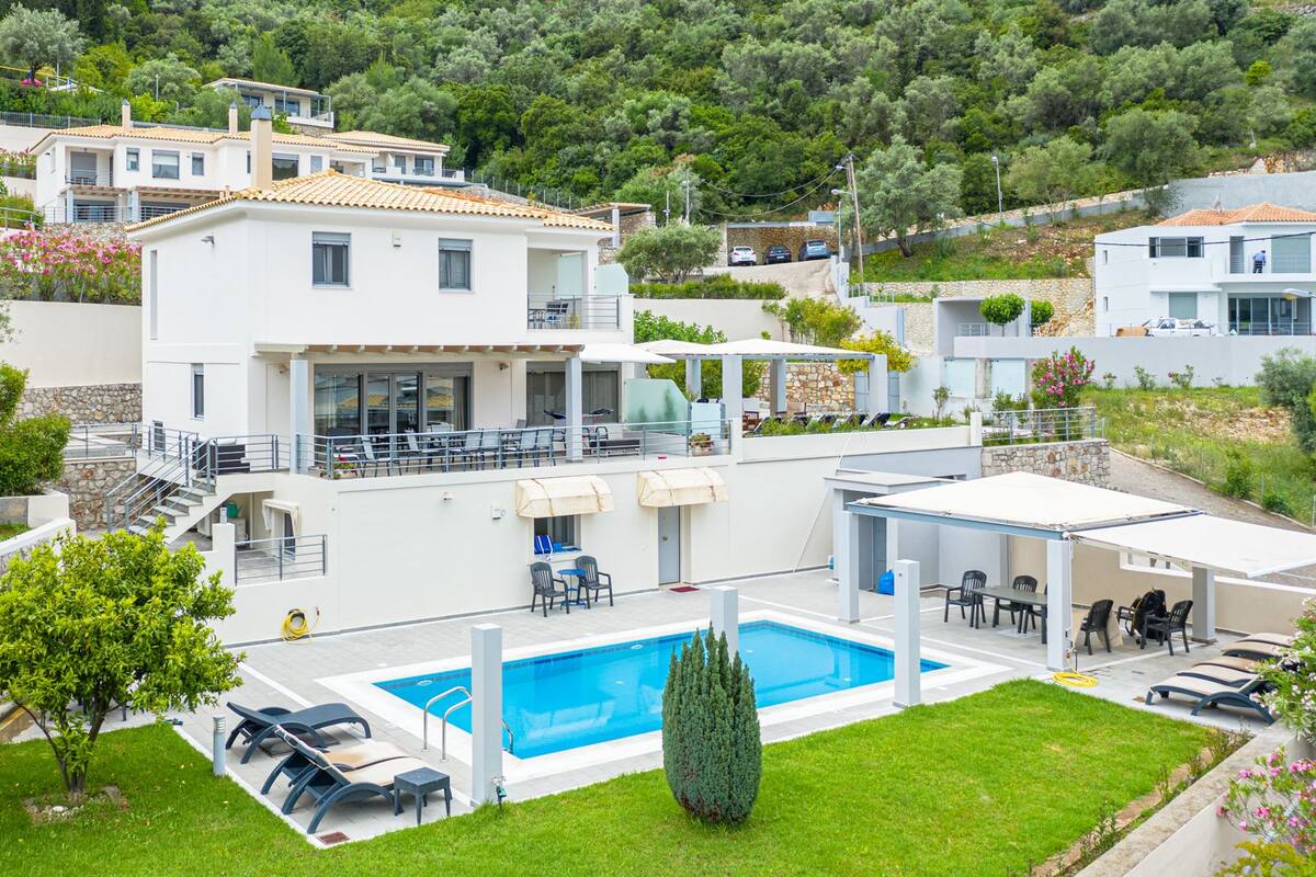 A modern villa with a swimming pool, outdoor seating, and a stone retaining wall.