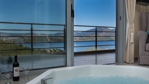A balcony with a view of a lake and mountains, a bathtub with bubbles, and a bottle of wine. - Thealos Village (Lefkada)