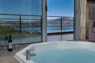 Un balcón con vistas a un lago y montañas, una bañera con burbujas y una botella de vino.