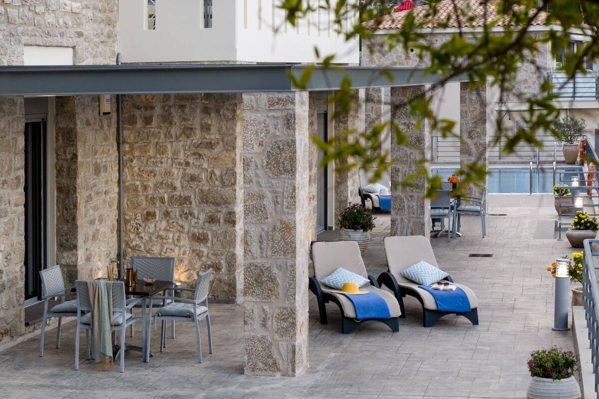 An outdoor seating area with stone walls, a table with chairs, and lounge chairs with cushions.