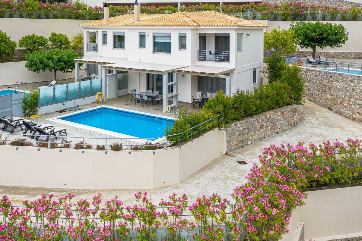 A two-story house with a swimming pool, outdoor seating, and a stone wall.