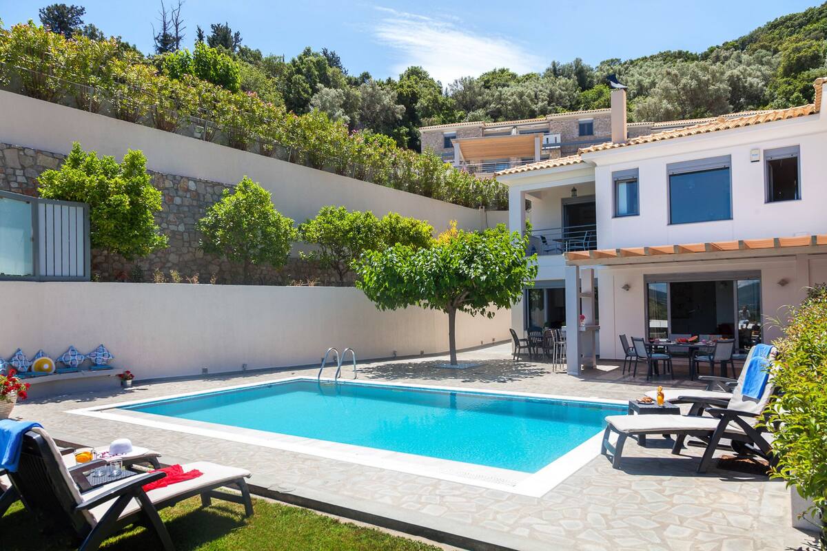 A swimming pool with lounge chairs, a table, and a patio area with a view of a hillside.