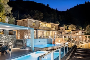 Un área de piscina lujosa con un muro de piedra, un jacuzzi y un comedor con asientos exteriores.