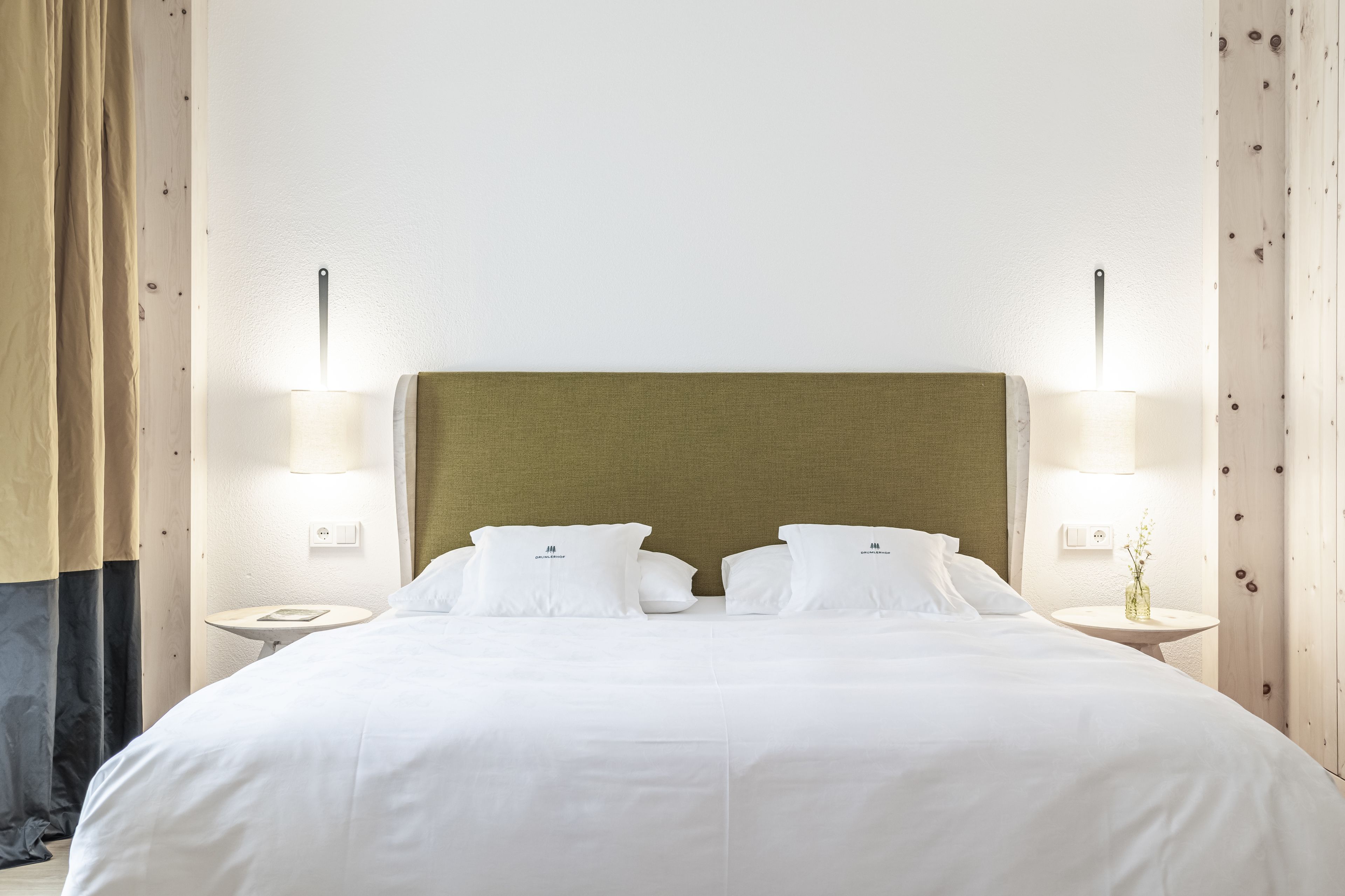 Ein ordentlich bezogenes Bett mit weißen Leinentüchern und zwei Kissen, an beiden Seiten mit Nachttischen und Lampen, in einem Zimmer mit Holzvertäfelung und schlichtem, klaren Design.