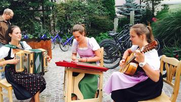 A group of people playing traditional instruments in an outdoor setting with bicycles and greenery in the background.