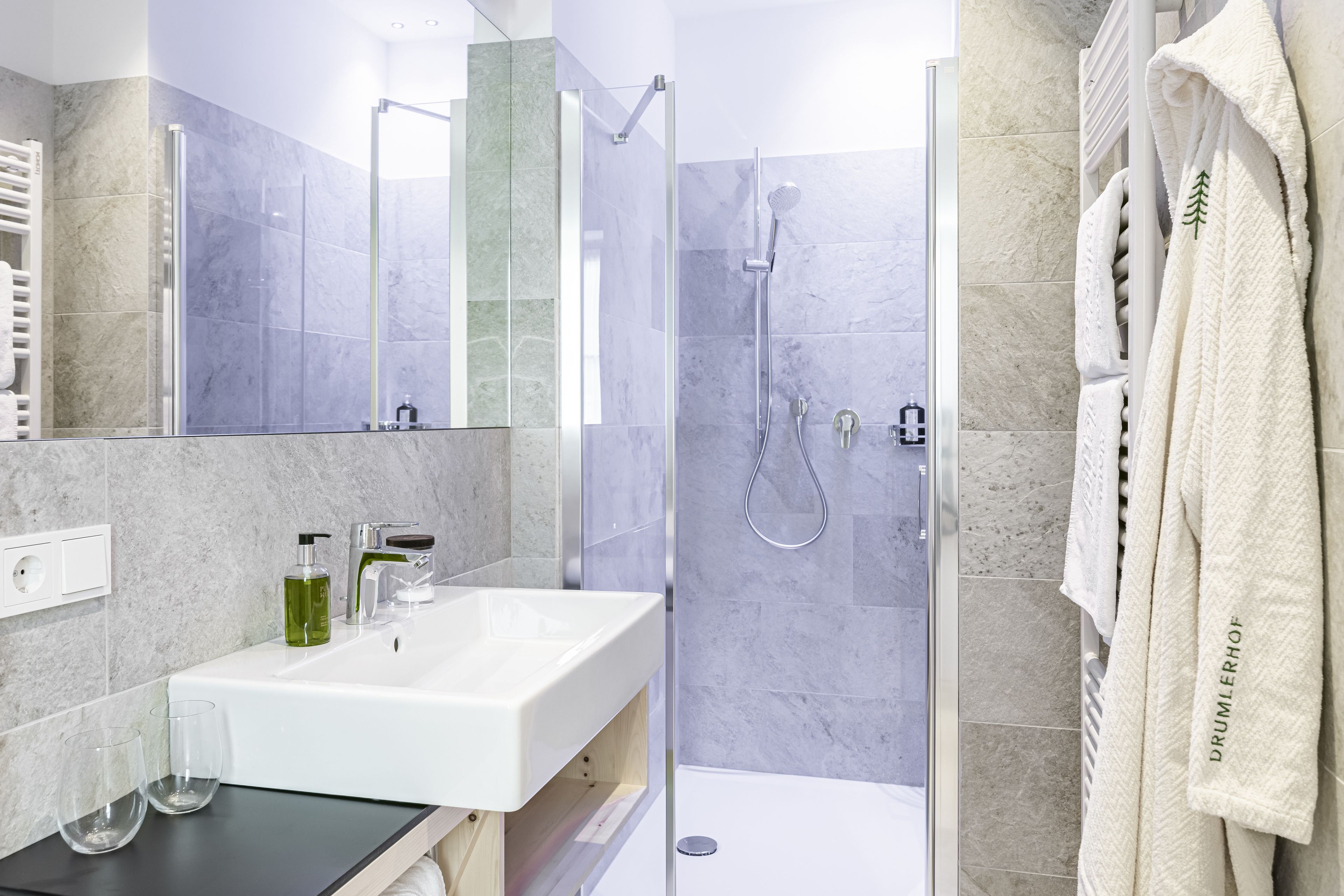 A modern bathroom with a glass-enclosed shower, a white sink, and a towel rack with a robe.