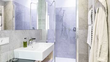 A modern bathroom with a glass-enclosed shower, a white sink, and a towel rack with a robe.