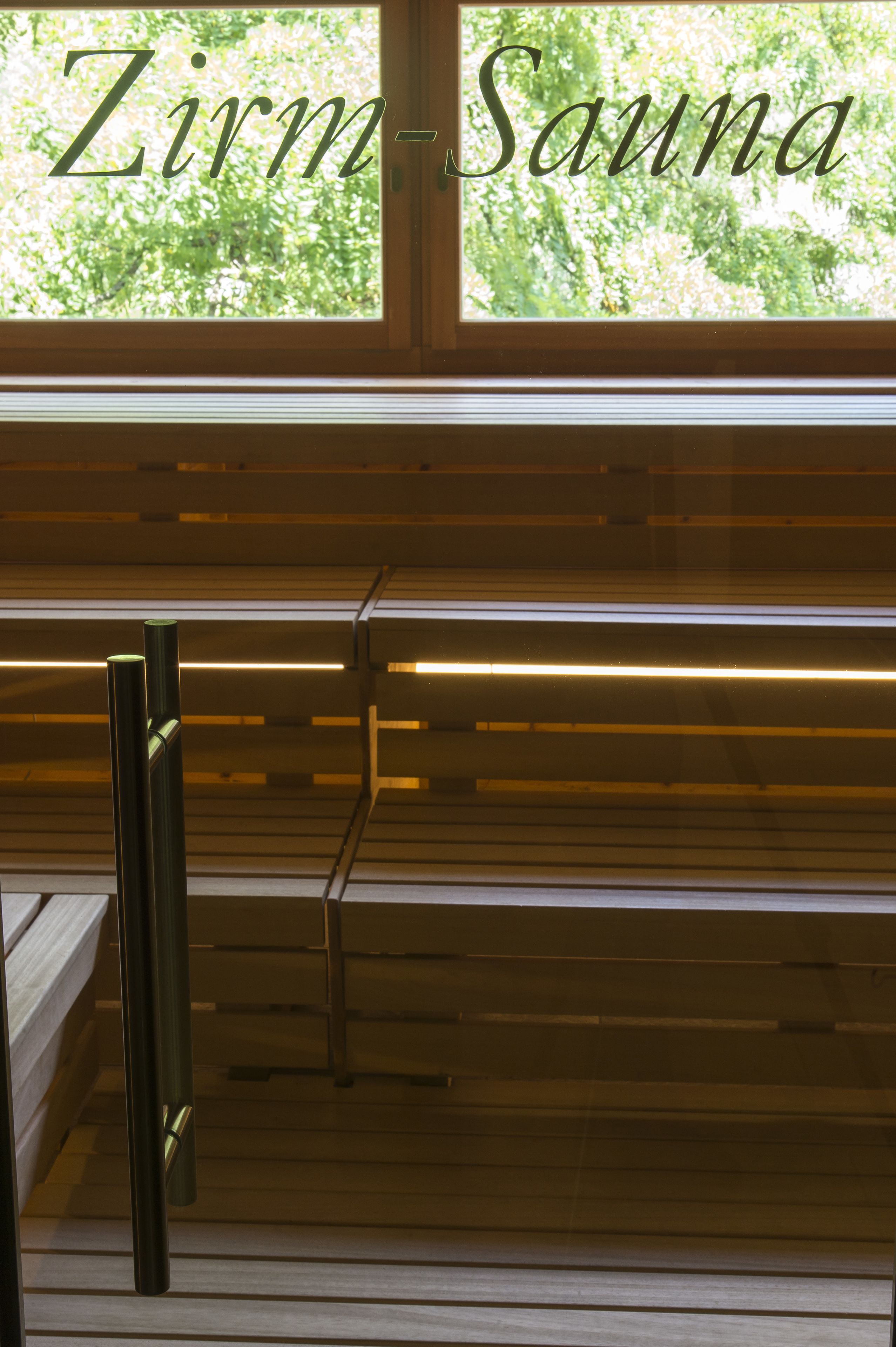 A wooden bench area with a window view, and the text "Zirm-Sauna" is visible.