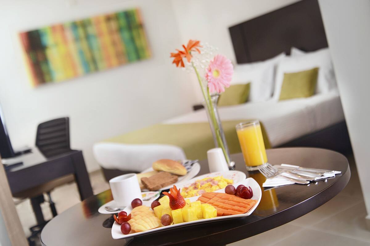 Una bandeja de desayuno con frutas, un vaso de jugo de naranja y un florero sobre una mesa en una habitación de hotel.