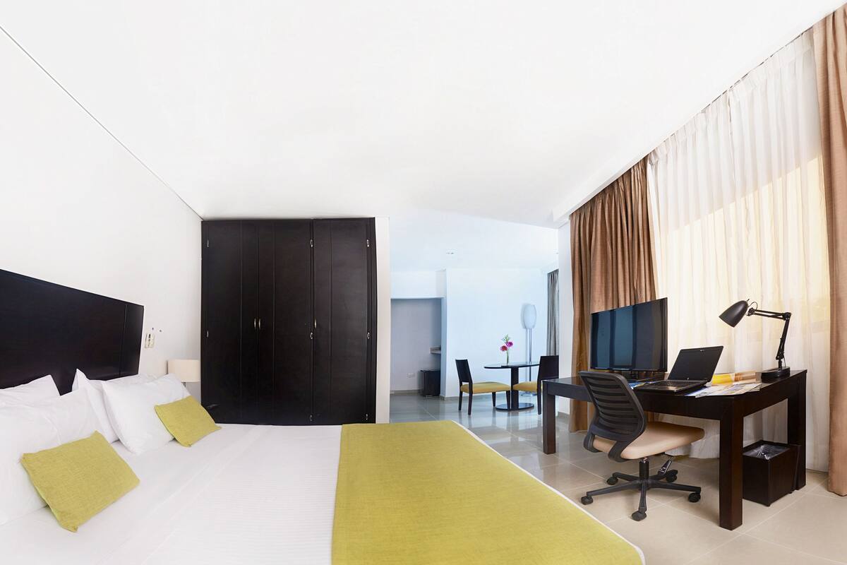 Una habitación de hotel con cama, escritorio, silla, televisor y lámpara.