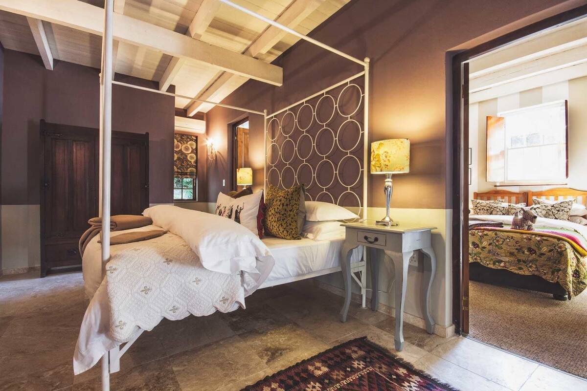 A bedroom with a four-poster bed, a bedside table with a lamp, and a patterned headboard.
