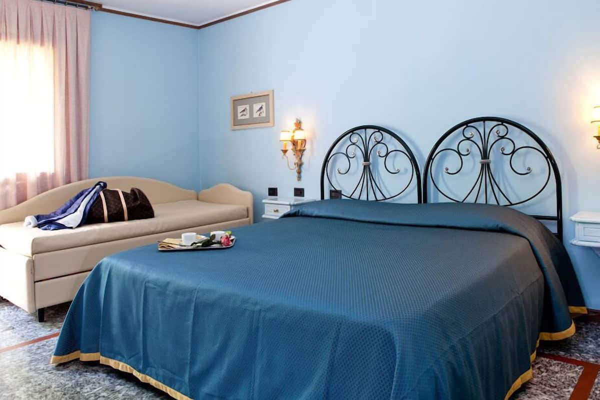 A bedroom with a bed, a sofa, a nightstand, and a wall-mounted lamp.