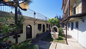 A courtyard with a stone pathway, a fountain, and a small garden area with palm trees. - Hotel Sport Daniel (Pescasseroli)