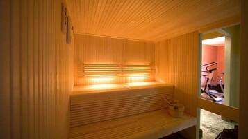 Una sauna con listones de madera y un banco, una ventana y una bicicleta estática visible en el exterior.