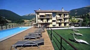 A hotel with a poolside area, wooden deck, and a view of mountains. - Hotel Sport Daniel (Pescasseroli)