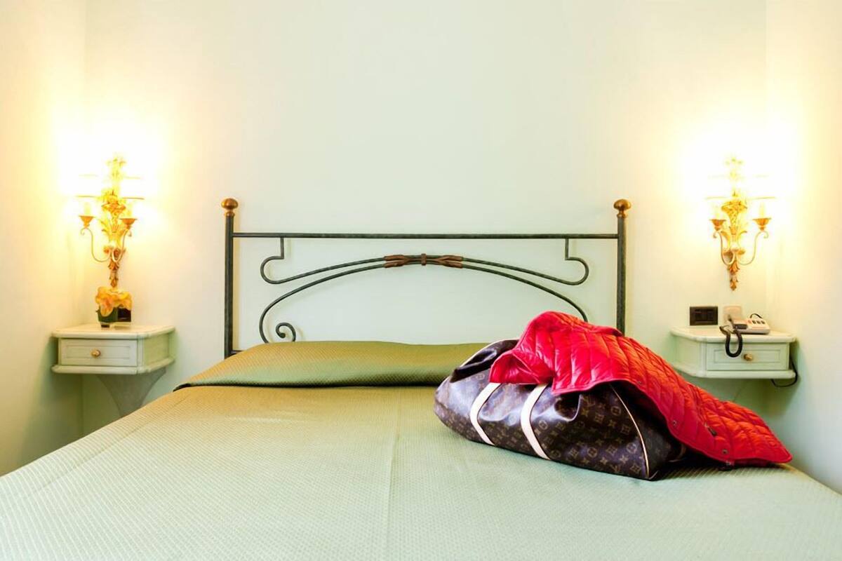 A bed with a green bedspread, a red and black bag on the bed, and two bedside tables with lamps.