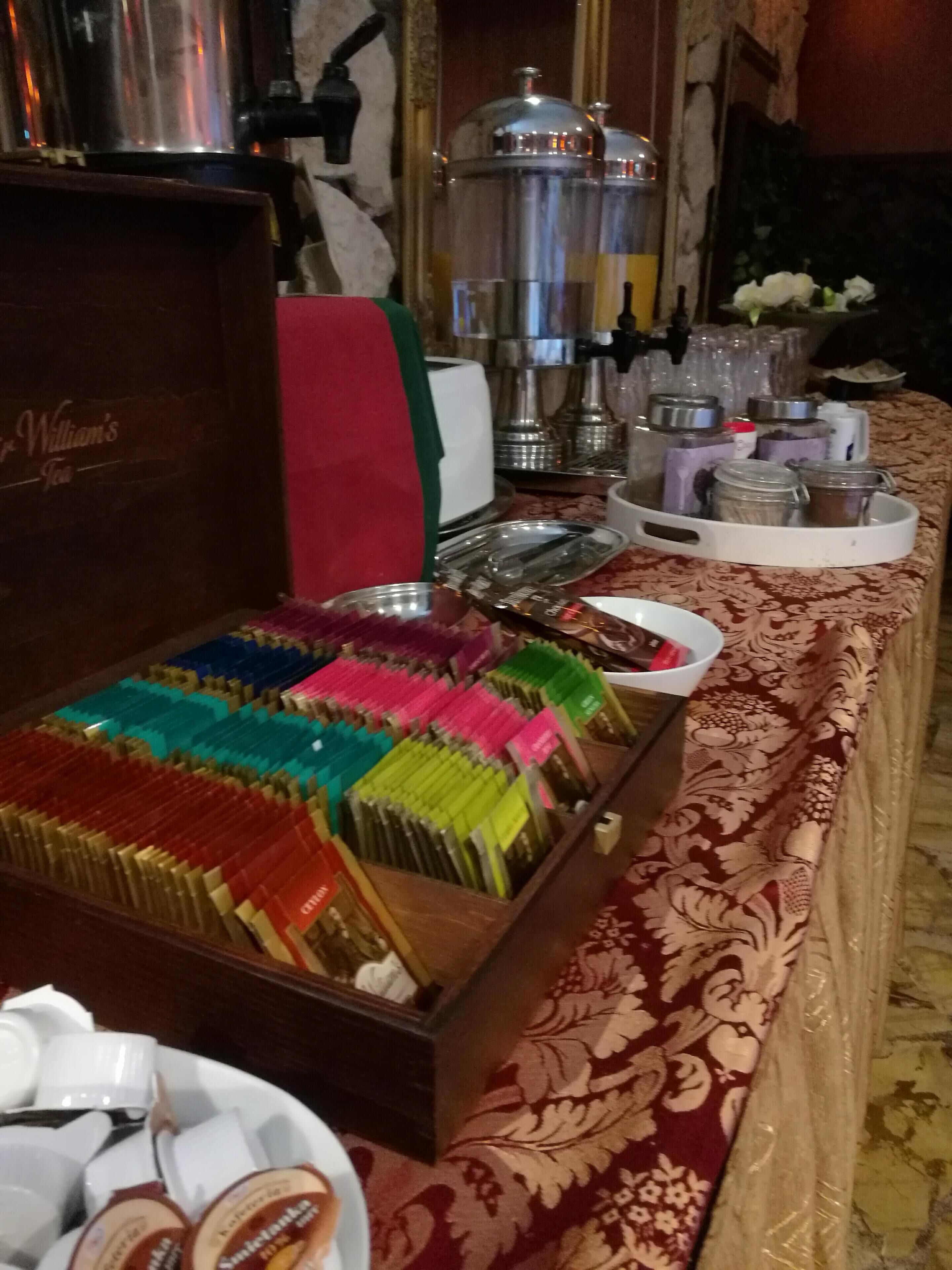 A buffet table with a variety of food items, including a large box of colorful napkins, a coffee station, and several condiment containers.