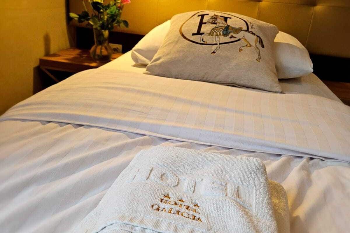A hotel room with a neatly made bed, a pillow with a horse logo, and a towel with hotel branding.