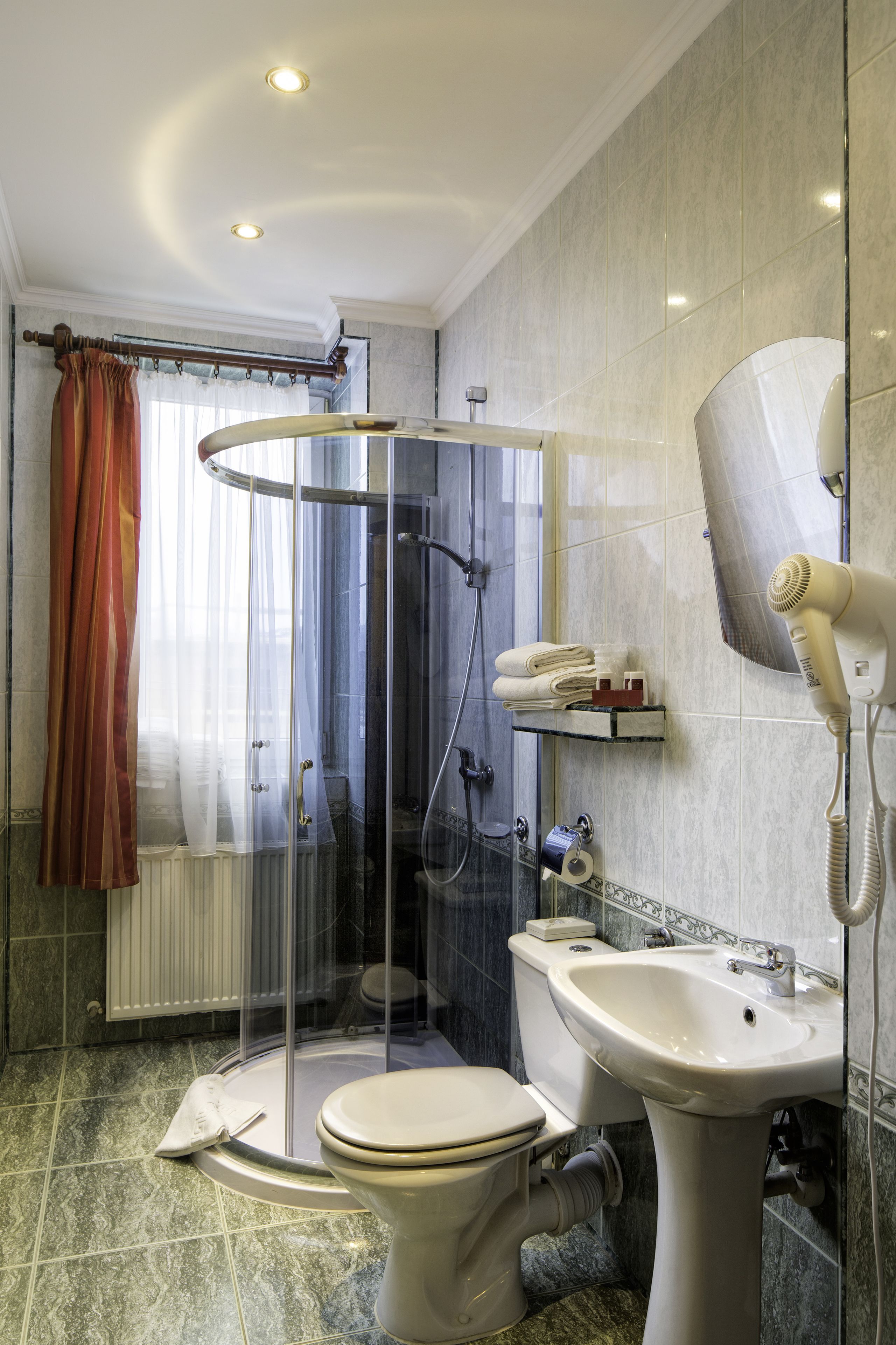 A bathroom with a toilet, sink, shower, and hairdryer.