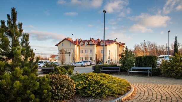 Hotelli, jossa on punainen katto, useita ikkunoita sekä kivetty alue, jossa on penkkejä ja viheralueita.