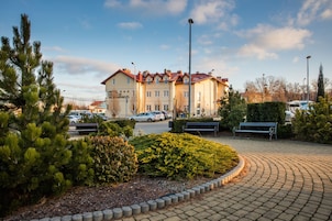 Um hotel com telhado vermelho, várias janelas e um espaço pavimentado com bancos e vegetação.