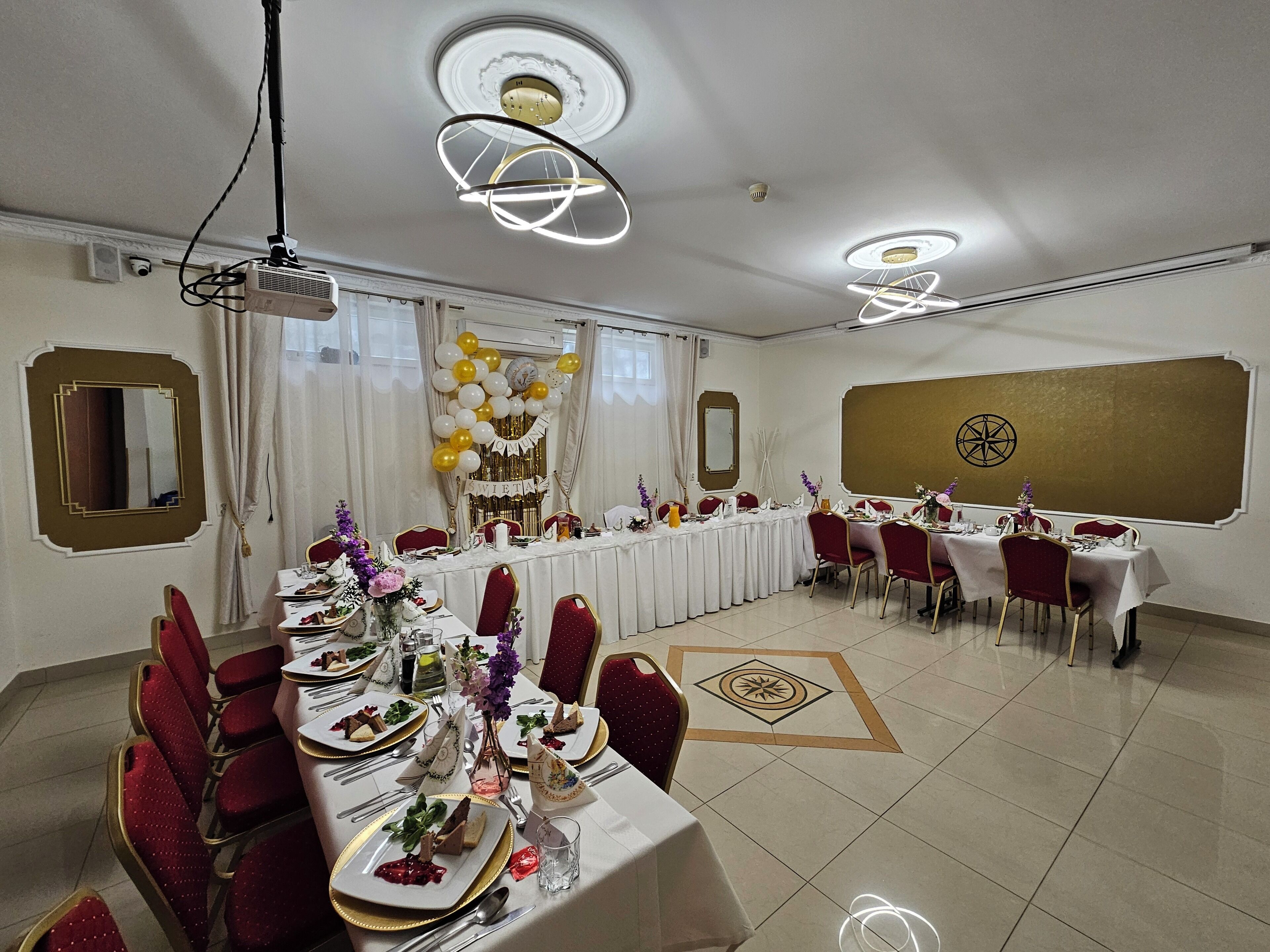 A banquet hall with round tables, red chairs, and a stage with a backdrop.