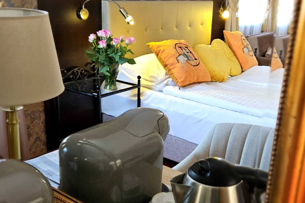 A hotel room with a bed, bedside lamps, a nightstand, a mirror, and a coffee maker.