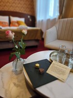 Quarto de hotel com uma cama, um sofá, uma mesinha com um vaso de flores, um tabuleiro com copos e um menu.