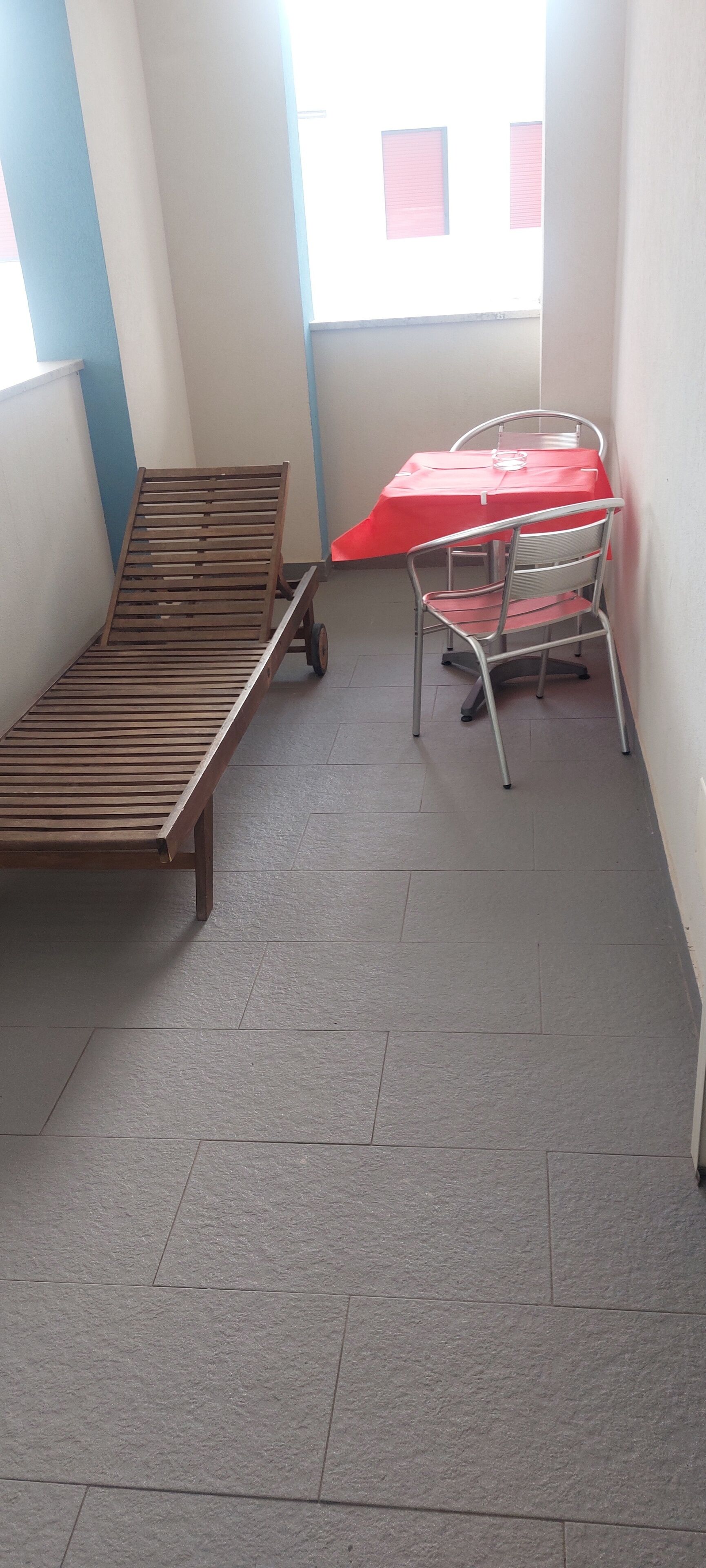 Una habitación pequeña con una cama de madera, una silla de metal y una mesa roja.