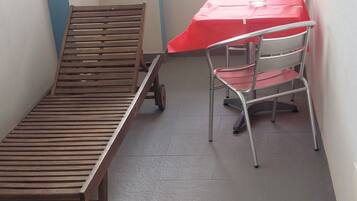 Una habitación pequeña con una cama de madera, una silla de metal y una mesa roja.