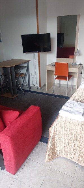A hotel room with a bed, a red sofa, a desk with a computer, a chair, a TV mounted on the wall, and a mirror. - Blue Sky Hotel (Melendugno)