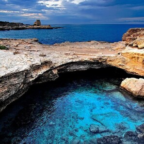 A coastal stone bridge leading to a clear blue sea with rocky formations. - Blue Sky Hotel (Melendugno)