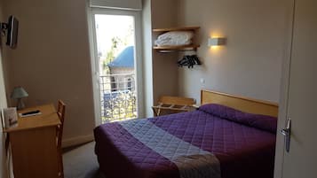 Habitación de hotel con cama, escritorio, silla, lámpara, armario y ventana con vistas al exterior.
