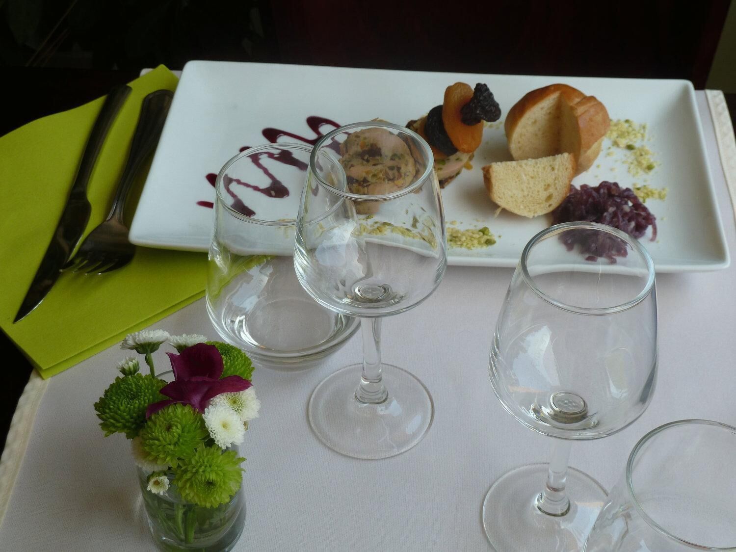 A dining table with a white plate, empty wine glasses, and a green napkin.