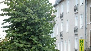 Hotelli, jonka edessä on suuri puu, ja jossa on keltainen kyltti, jossa lukee sana ”HOTEL”, sekä valkoisilla ikkunoilla ja parvekkeilla varustettu rakennus.