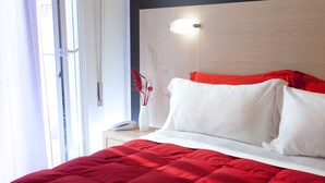 Una cama bien hecha con colcha roja, almohadas blancas y cabecera de madera con lámpara.