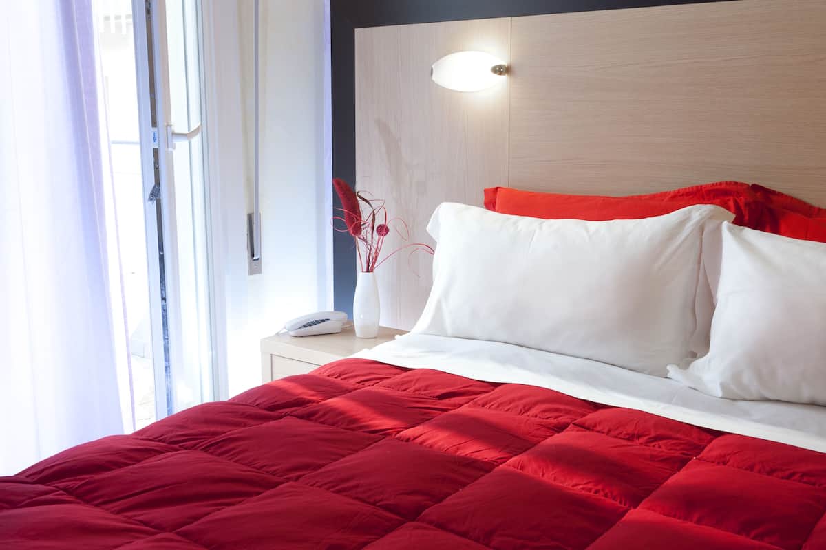 A neatly made bed with a red quilt, white pillows, and a wooden headboard with a light fixture.