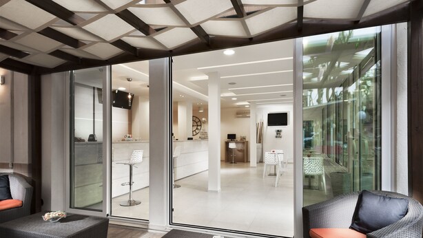 Una habitación de hotel moderna con una puerta de cristal que da a un balcón, una zona de estar con una mesa y un televisor montado en la pared.