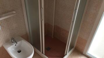 A bathroom with a glass-enclosed shower, a white sink, and tiled walls.