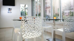 Un interior moderno con sillas y mesas blancas, un televisor de pantalla plana en la pared y ventanas amplias con vistas al exterior.