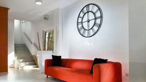 Un vestíbulo moderno con un sofá rojo, un reloj de pared grande y una escalera.