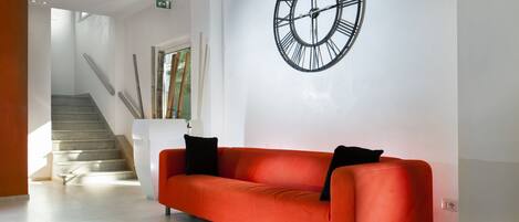 Un vestíbulo moderno con un sofá rojo, un reloj de pared grande y una escalera.