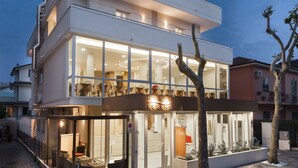 Un hotel moderno con fachada de vidrio, varios pisos y un área de restaurante visible.