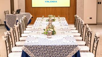 Een vergaderruimte in Hotel Finlandia met een lange tafel gedekt voor een vergadering, witte stoelen en een projectiescherm waarop het logo van het hotel staat.