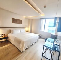 Une chambre d’hôtel moderne avec un grand lit, des tables de chevet, un bureau et une fenêtre équipée de stores.