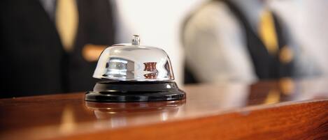 A hotel reception area with a wooden reception desk and a bell.
