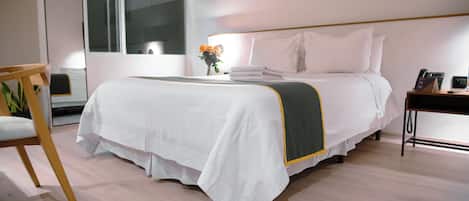 A neatly made bed with a white and green bedspread, a bedside table with a phone and a small plant, and a chair with a wooden frame.