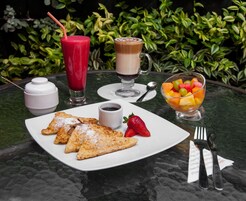 Une table avec des aliments pour le petit-déjeuner, notamment des crêpes, un saladier de fruits, une boisson au café et un smoothie.