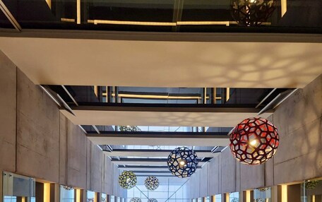 A modern architectural interior with a geometric design, featuring a central glass corridor and hanging spherical light fixtures.