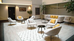 A modern lobby with a geometric patterned rug, white armchairs, a sofa with yellow cushions, and a potted plant. - Hotel Finlandia (Quito)